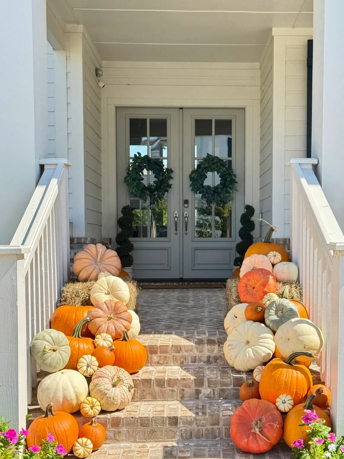 Heirloom and orange pumpkins lining a white porch with double doors and wreaths