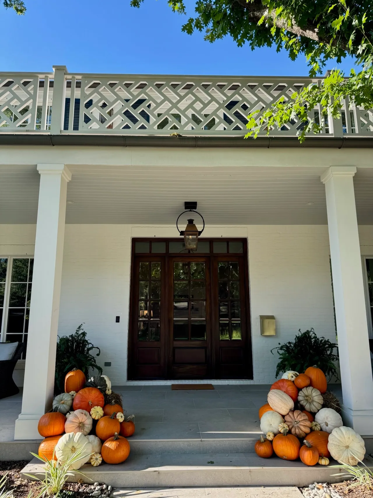 Twin pumpkin piles flanking the steps of a white brick home with a wood front door